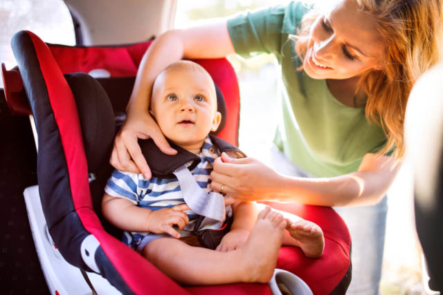 Young Mother Putting Baby Boy in Harness Car Seat